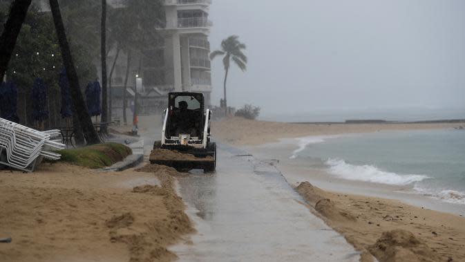 Traktor kecil mendorong pasir dari jalan setapak di Pantai Waikiki, Honolulu  (6/12/2021). Pihak berwenang mengatakan kondisi yang berpotensi lebih buruk ke depannya. (AP Photo/Marco Garcia)