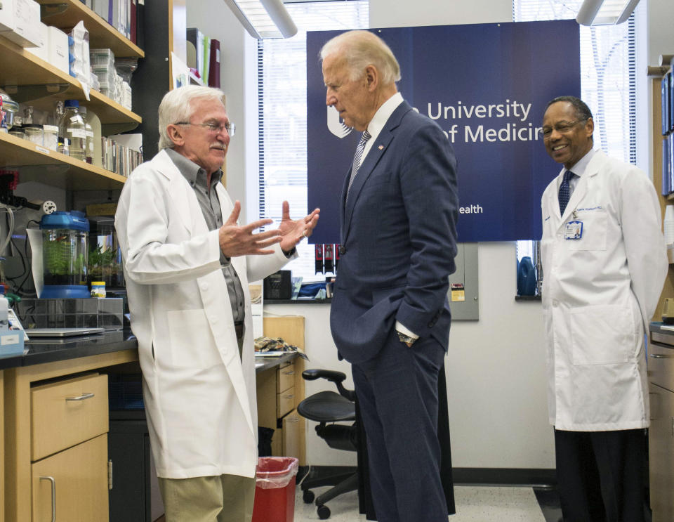 FILE - In this Feb. 10, 2016 file photo, Vice President Joe Biden speaks with Nobel Laureate Dr. Paul Modrich, left, as Dr. A. Eugene Washington, Chancellor for Health Affairs at Duke University, right listens in a laboratory at Duke University School of Medicine in Durham, N.C. Biden’s defining venture since leaving the Obama White House is the Biden Cancer Initiative, a nonprofit aimed at speeding a cancer cure in memory of his son. (AP Photo/Ben McKeown)