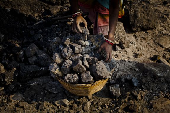 A woman stacks coal into a basket as she and others work to scavenge coal from an open-cast coal mine in Jharia, India.