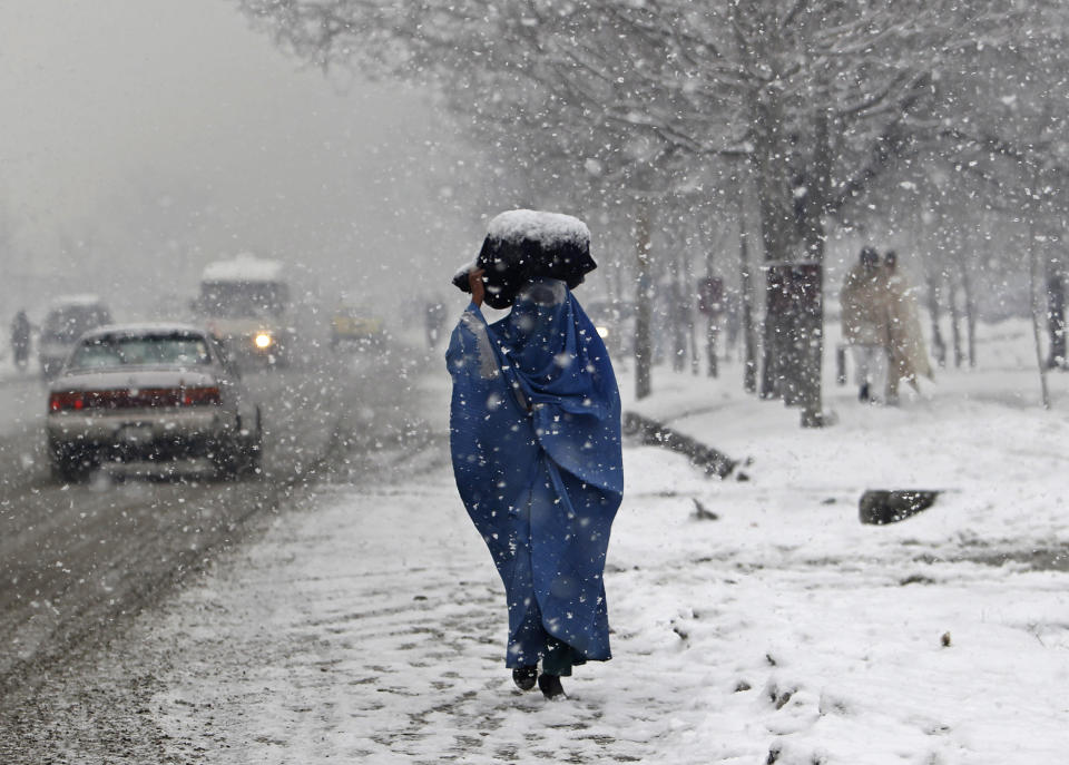 A woman carries a sack on her head along a street on a snowy day in Kabul