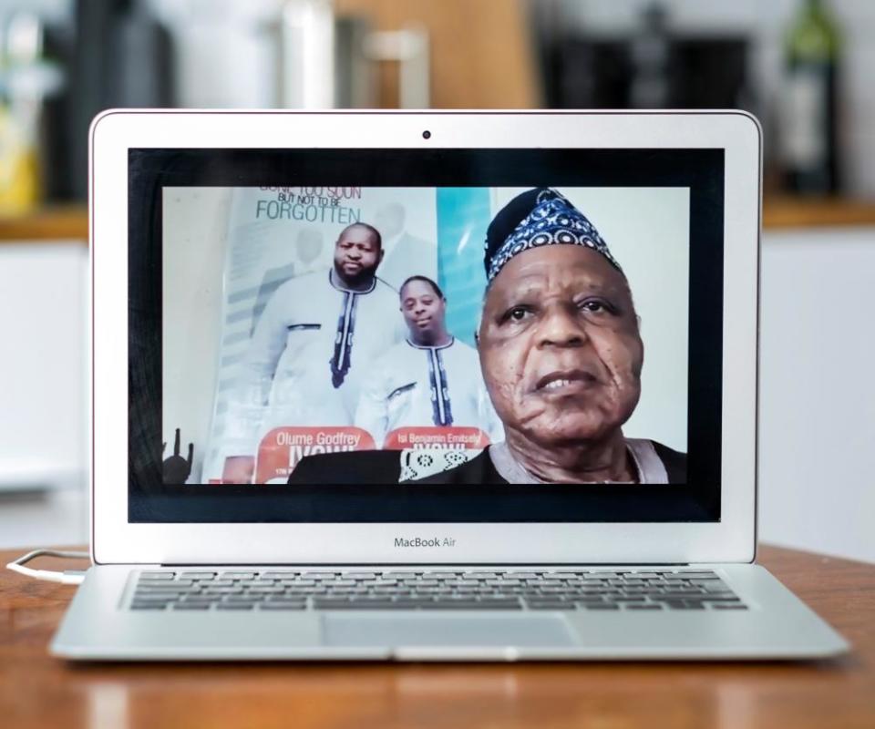 A Zoom portrait of Sir Oyaseh Ivowi; behind him is a poster of two of his sons, Olume (left) and Isi.