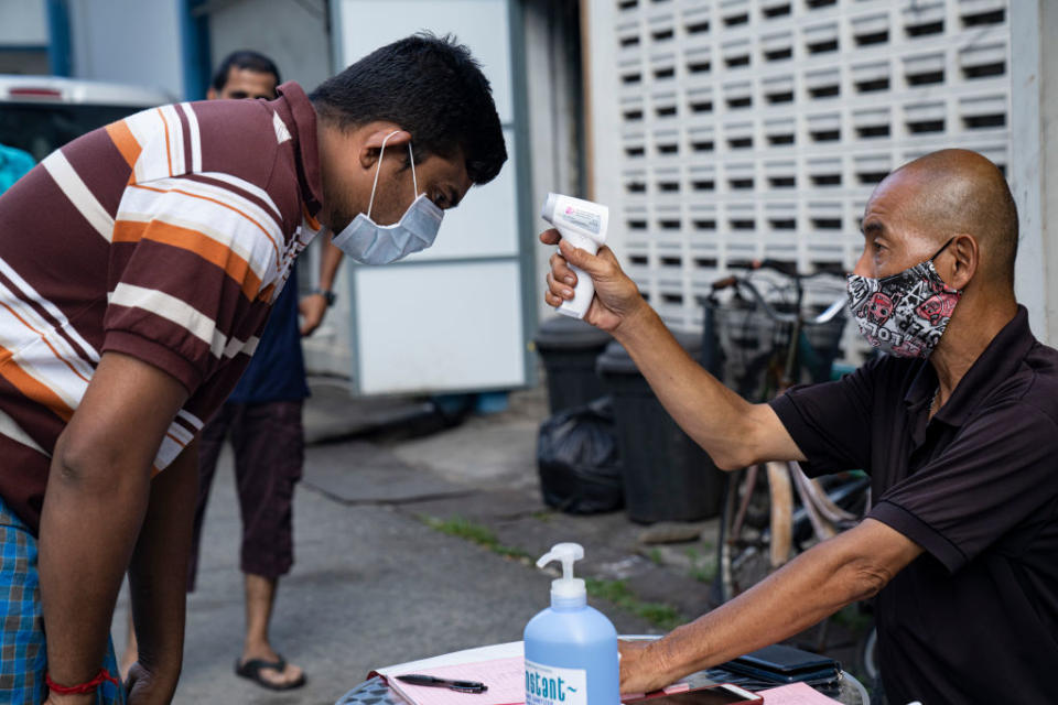 A migrant worker has his temperature checked by a security guard before leaving a factory-converted dormitory in Singapore on April 17, 2020. | Ore Huiying—Getty Images