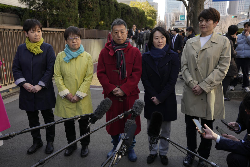 One of the plaintiffs, with a navy scarf, fourth left, speaks before media members by the main entrance of the Tokyo district court before hearing the ruling regarding LGBTQ+ marriage rights, in Tokyo, Thursday, March 14, 2024. The Japanese court on Thursday ruled that not allowing same-sex couples the same marital benefits as heterosexuals violates their fundamental right to have a family, but the current civil law did not take into consideration sexual diversity and is not clearly unconstitutional, a partial victory for Japan's LGBTQ+ community calling for equal marriage rights. (AP Photo/Hiro Komae)