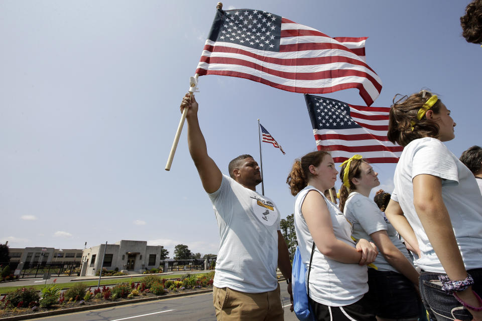 Amaad Rivera, of Springfield, Mass., left, holds an American flag during a rally in front of the headquarters of gun manufacturer Smith & Wesson, behind left, in Springfield, Sunday, Aug. 26, 2018. The march, held to call for gun law reforms, began Thursday, Aug. 23, 2018, in Worcester, Mass., and ended Sunday, in Springfield, near the gun manufacturer. (AP Photo/Steven Senne)