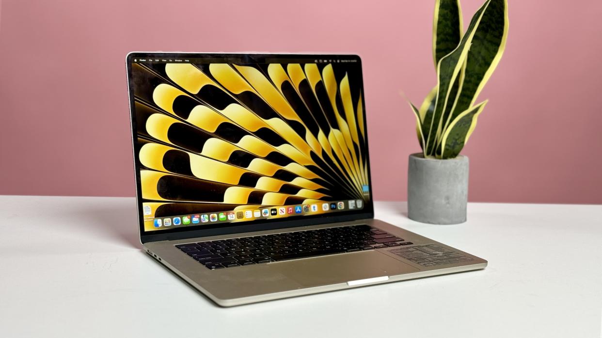  MacBook Air 15 M2 in silver open on a white desk facing you with a pink wall behind it. 