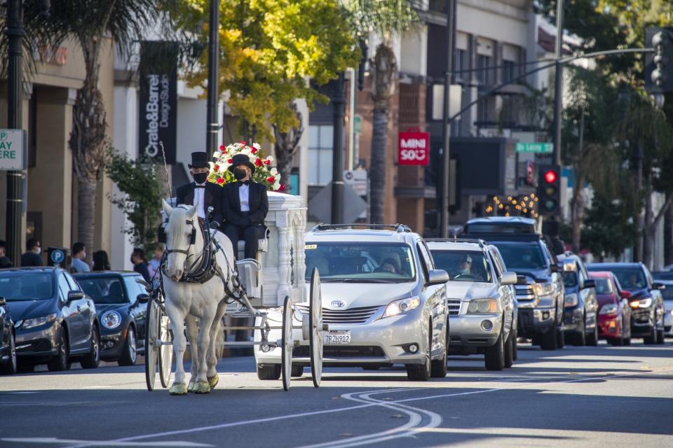 A horse-drawn carriage leads a funeral procession down Colorado Boulevard in Pasadena.