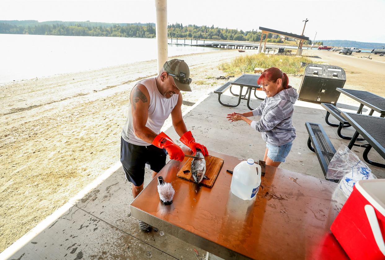 Greg Donaldson begins to scale a coho salmon while his partner Lisa DeCoteau washes her hands as they clean their freshly caught dinner on the stainless steel table in the new multi-purpose picnic shelter on the shore of Port Gamble S'Klallam Tribe’s Point Julia on Tuesday, Sept. 5, 2023.