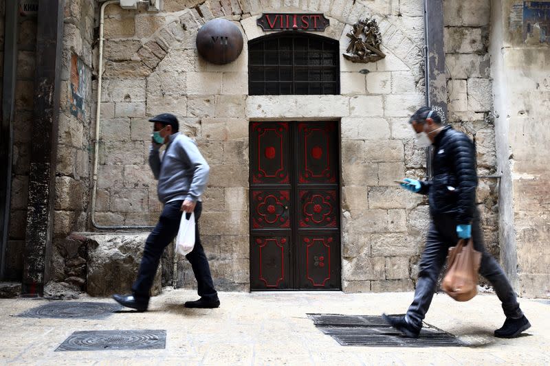 People wearing masks walk past a bronze sculpture by Italian artist Alessandro Mutto at one of the Stations of the Cross along the Via Dolorosa, amid the coronavirus disease (COVID-19) outbreak in Jerusalem's Old City