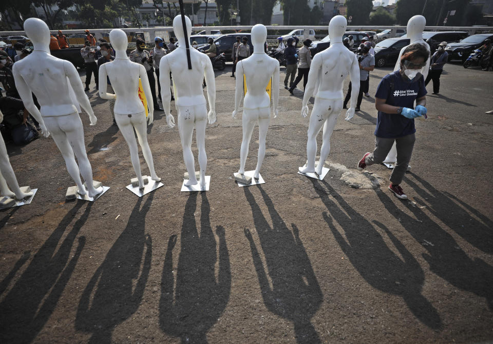 A Greenpeace activist walks past mannequins used to display posters during a protest outside the parliament in Jakarta, Indonesia, Monday, June 29, 2020. About a dozen of activists staged the protest against the government's omnibus bill on job creation that was intended to boost economic growth and create jobs, saying that it undermined labor rights and environmental protection. (AP Photo/Dita Alangkara)