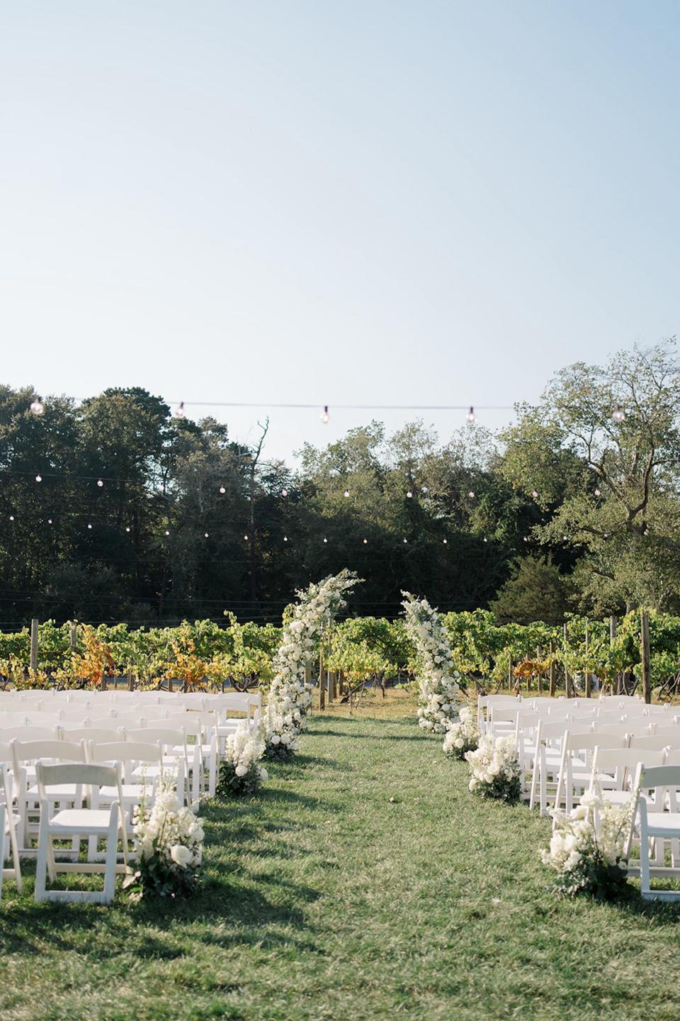 An outdoor wedding in front of a vineyard with a floral arch at the aisle.