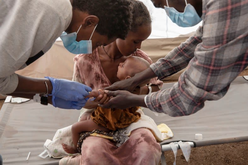 In this Dec. 5, 2020 file photo, a Tigray woman who fled the conflict in Ethiopia’s Tigray region, holds her malnourished and severely dehydrated baby as nurses give him IV fluids, at the Medecins Sans Frontieres (MSF) clinic, at Umm Rakouba refugee camp in Qadarif, eastern Sudan. (AP Photo/Nariman El-Mofty)