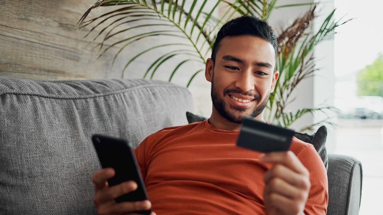 man on his sofa holding his phone and looking at a card
