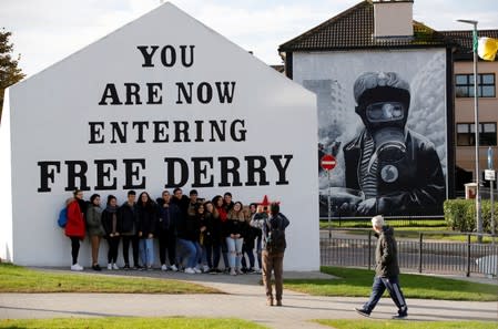 People pose for a photograph in front of a mural in the Bogside area of Londonderry, Northern Ireland