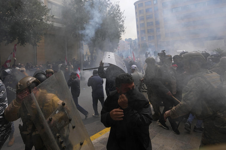 Retired members of the Lebanese security and other protesters run amid tear gas fired by riot police after the protesters try to remove barbed-wire barrier in order to advance towards the government building during a protest demanding better pay in Beirut, Lebanon, Wednesday, March 22, 2023. Lebanese security forces fired tear gas to disperse hundreds of protesters who tried to break through the fence leading to the government headquarters in downtown Beirut Wednesday amid widespread anger over the harsh economic conditions in the country. (AP Photo/Hassan Ammar)