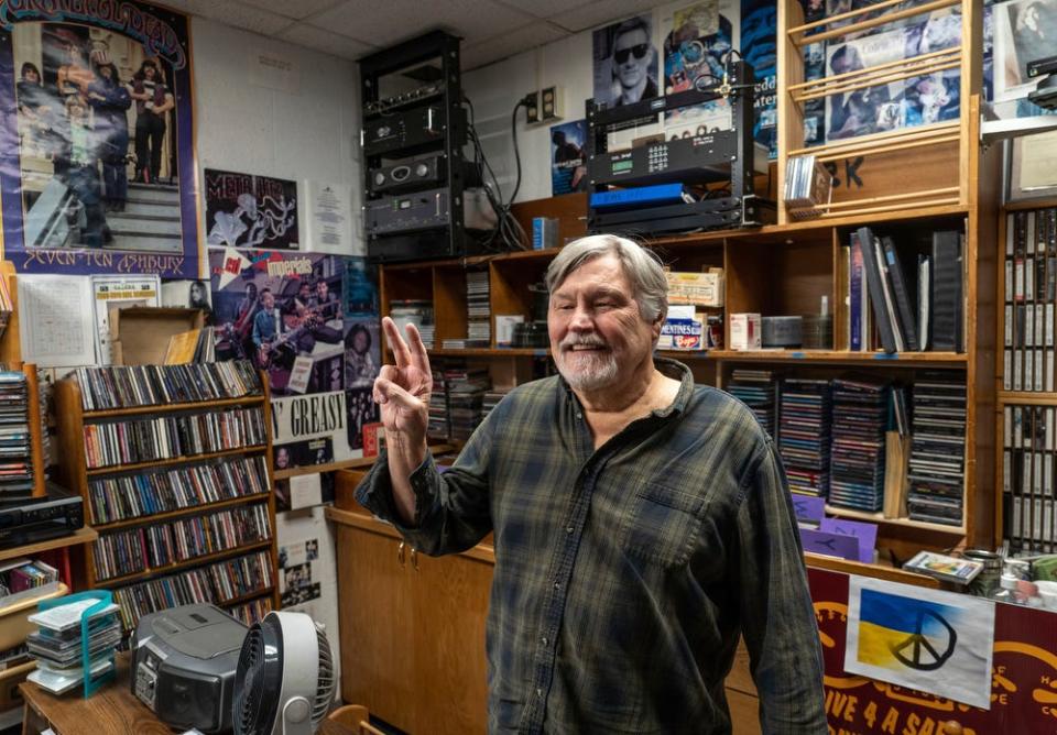 Lee McCaffrey, 71, the host of "Eclectic Fridays" on WOAS 88.5-FM, flashes the peace sign inside the station's booth on Monday, April 24, 2023. After 45 years, the station's frequency was recently taken by a larger station in Marquette. “It’s kind of like just a takeover,” McCaffrey said. “That’s something that I’m not too happy with at all. We’re not that powerful anyway. We would like to be, but I know there’s a limit you can go. We’re almost like pirate radio.”