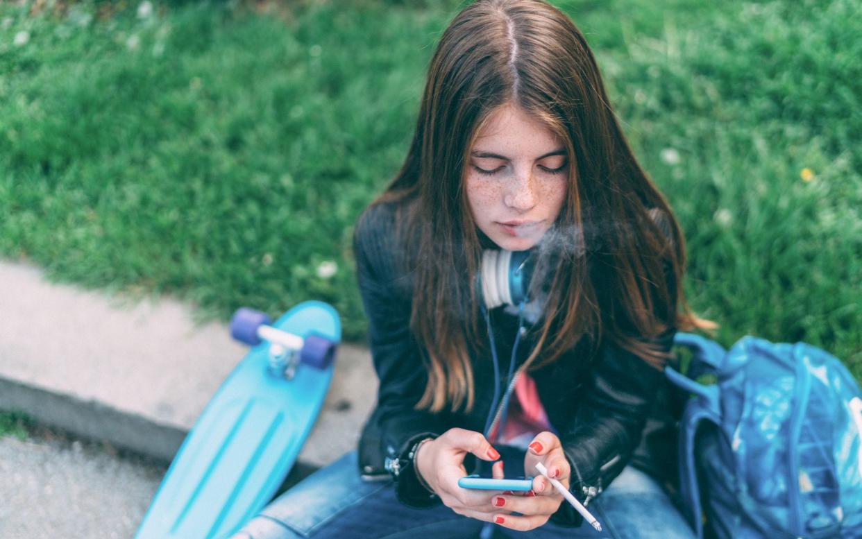 Teenage girl using smartphone outside while smoking