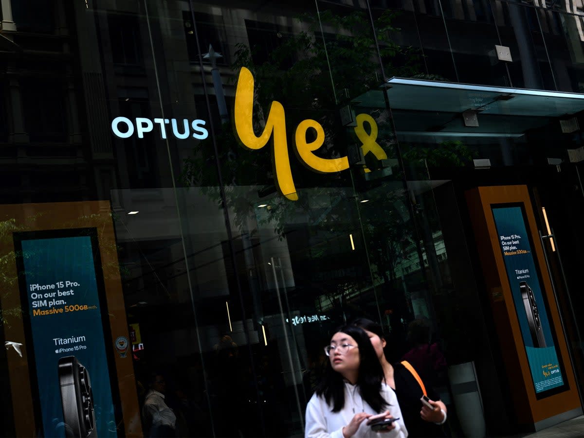 Girls browse on their mobile phones in front of Australian communications company Optus outlet in the central business district of Sydney on 8 November 2023 (AFP via Getty Images)
