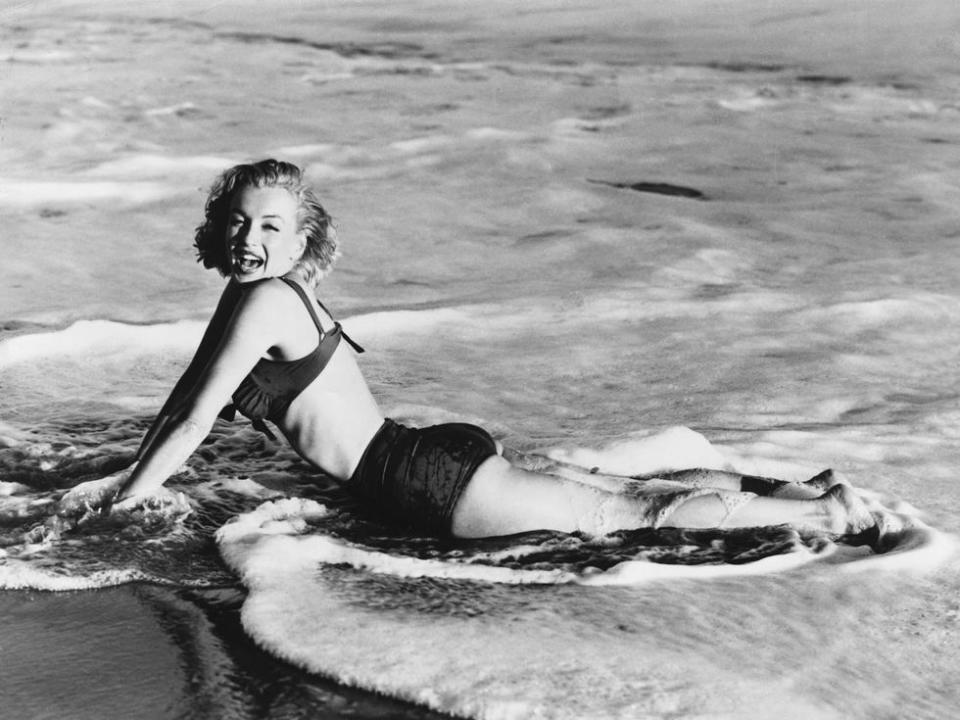 <p>Marilyn Monroe lays in the water as waves crash upon the shore in 1955.</p>