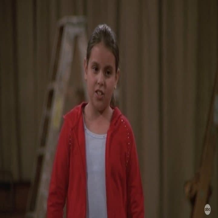 A young Beanie Feldstein with a ponytail in her hair in a red hoodie
