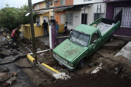 A pickup truck is seen after a street was damaged due to heavy rains, as residents look at damages in Veracruz September 2, 2014. REUTERS/Jonatan Rosas