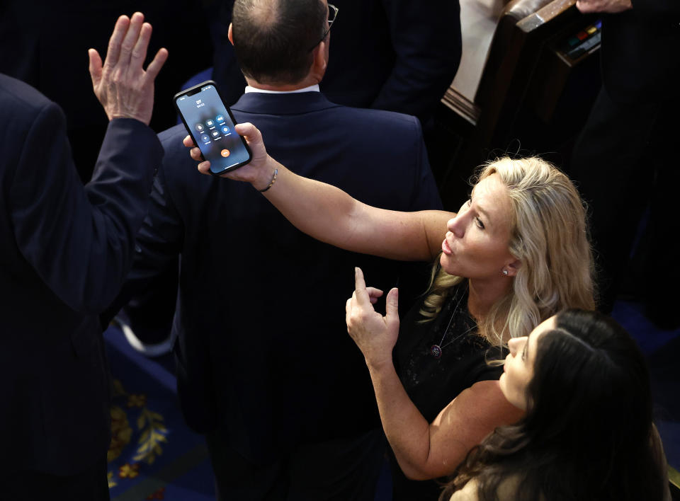 Marjorie Taylor Greene (R-GA) offers a phone with the initials “DT” to Matt Rosendale (R-MT), a Kevin McCarthy holdout, in the House Chamber.