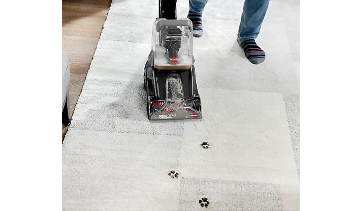 man using Bissell carpet cleaner on rug with dirty paw prints