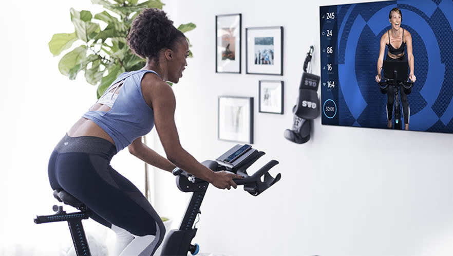 Woman on a connected stationary bike watching a spinning instructor on a television on the wall..