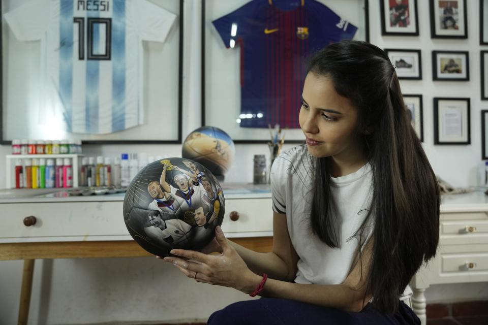 La artista plástica paraguaya Lili Cantero sostiene un balón de fútbol pintado a mano e ilustrado con integrantes de la selección de Alemania que disputó la Copa del Mundo de 2014, en San Lorenzo, Paraguay, el jueves 10 de noviembre de 2022. (Foto AP/Jorge Sáenz)