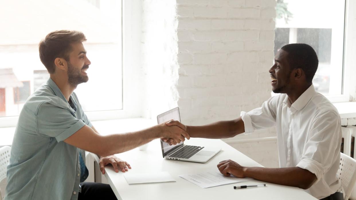 Satisfied happy african and caucasian partners shaking hands signing contract after giving bribe, smiling corrupted diverse businessmen closing deal with handshake, forming multiracial partnership.