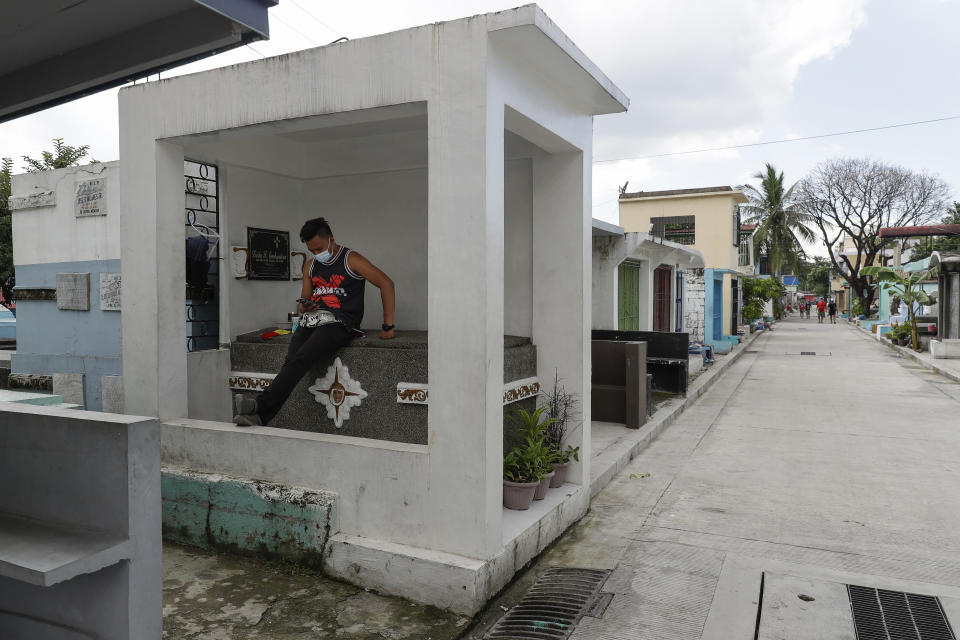 A man wearing a facemask to prevent the spread of the coronavirus sits on top of the tomb of a relative at Manila's North Cemetery, Wednesday, Oct. 28, 2020, in Manila, Philippines. The government has ordered all private and public cemeteries, memorial parks, and columbariums to be closed from Oct. 29 to Nov. 4, 2020, to prevent people from gathering during the observance of the traditionally crowded All Saints Day and to help curb the spread of the coronavirus. (AP Photo/Aaron Favila)