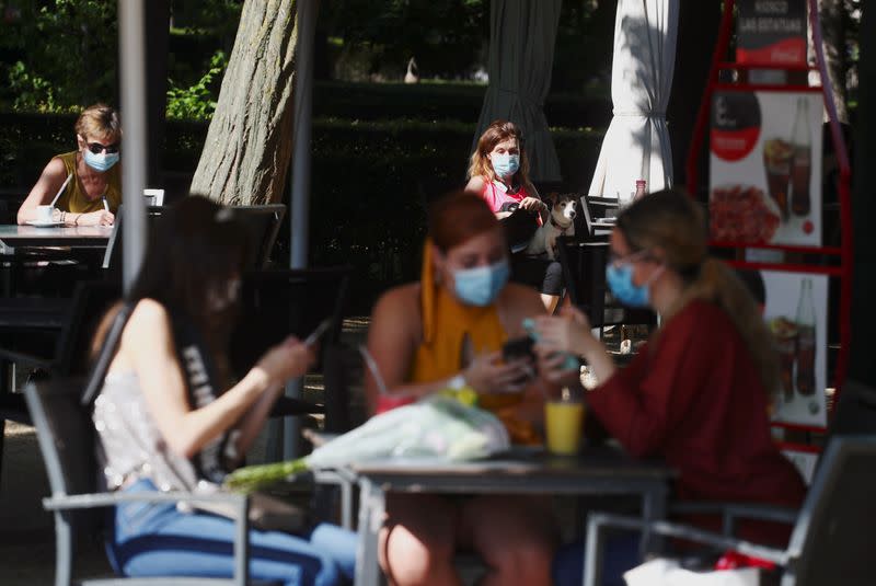 People wearing face masks sit at an outdoor seating section of a kiosk at Retiro Park as it is reopened for the first time in more than 2 months in Madrid