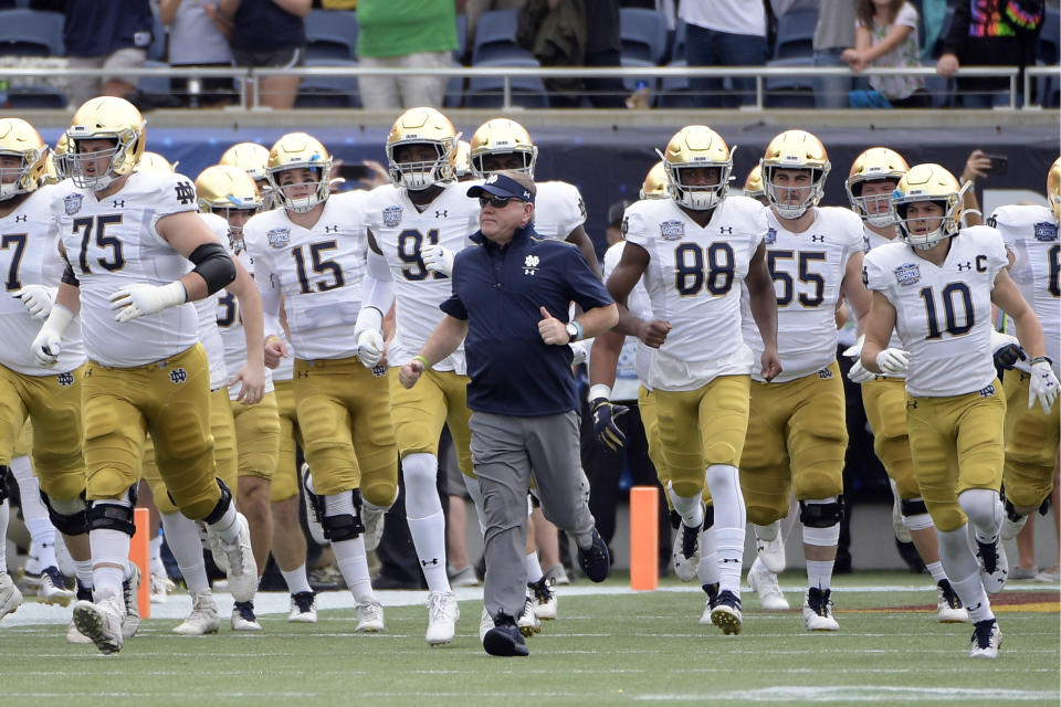 FILE - In this Dec. 28, 2019, file photo, Notre Dame head coach Brian Kelly, center, runs onto the field with his players before the Camping World Bowl NCAA college football game against Iowa State in Orlando, Fla. The Atlantic Coast Conference and Notre Dame are considering whether the Fighting Irish will give up their treasured football independence for the 2020 season play as a member of the league. (AP Photo/Phelan M. Ebenhack, File)