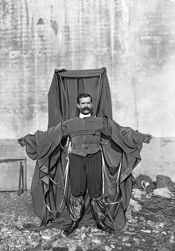 A man in a black-and-white photo with a large piece of cloth attached to his suit with several straps