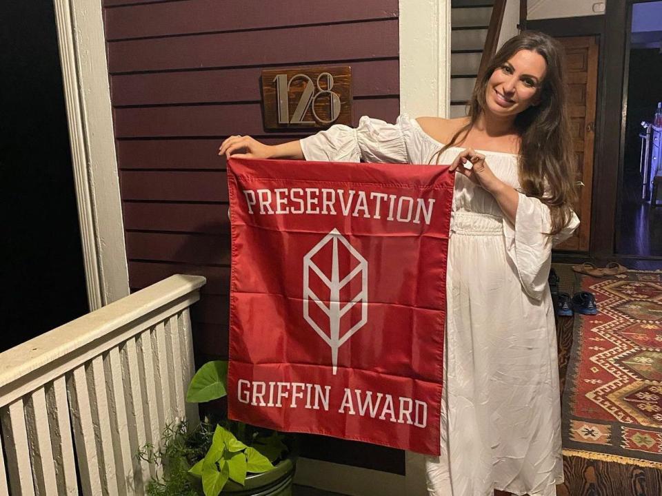 Paige Baratta holding up a banner for the preservation award that the couple won for their work on the house.