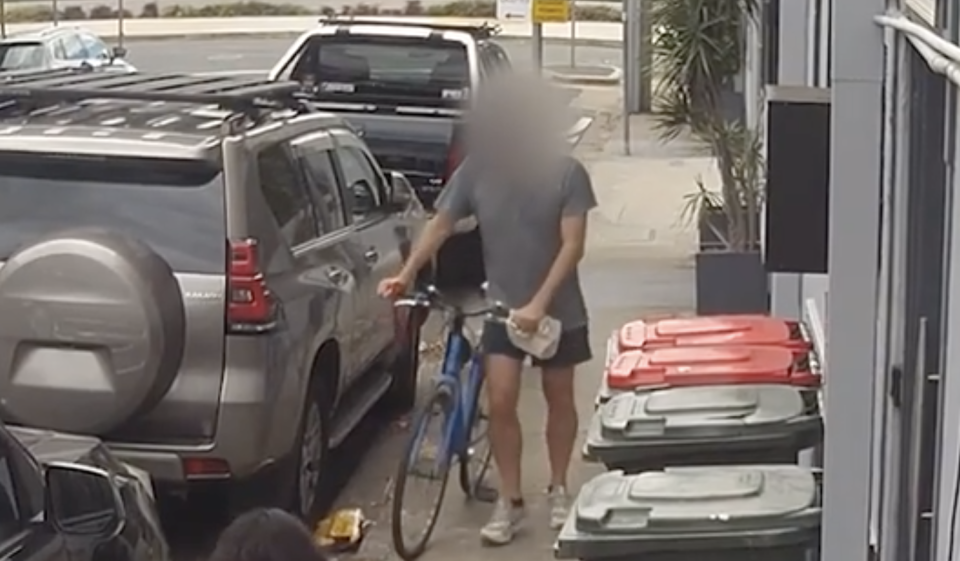 The cyclist walking his blue bike back up Hubert Street in Woolloongabba next to the keyed cars. 