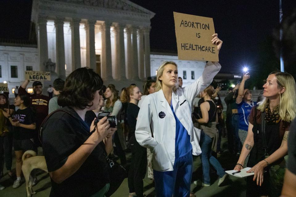 Abortion rights activist rally around a woman, dressed as a doctor, holding up a sign that reads "Abortion is healthcare," during a protest outside the Supreme Court.