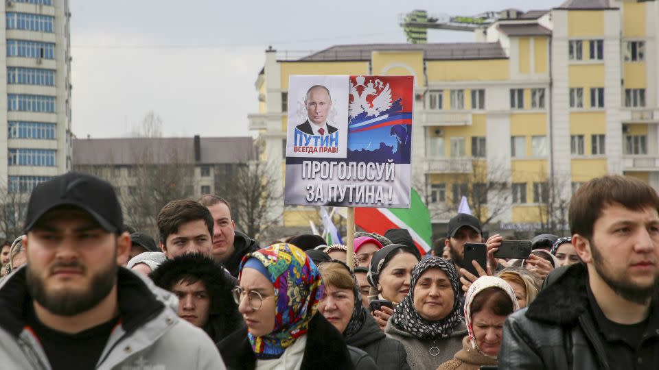 People take part in an election event in the Chechen capital Grozny, Russia. The slogan next to Putin on the poster reads: "Putin is always right! Vote for Putin!" - Chingis Kondarov/Reuters
