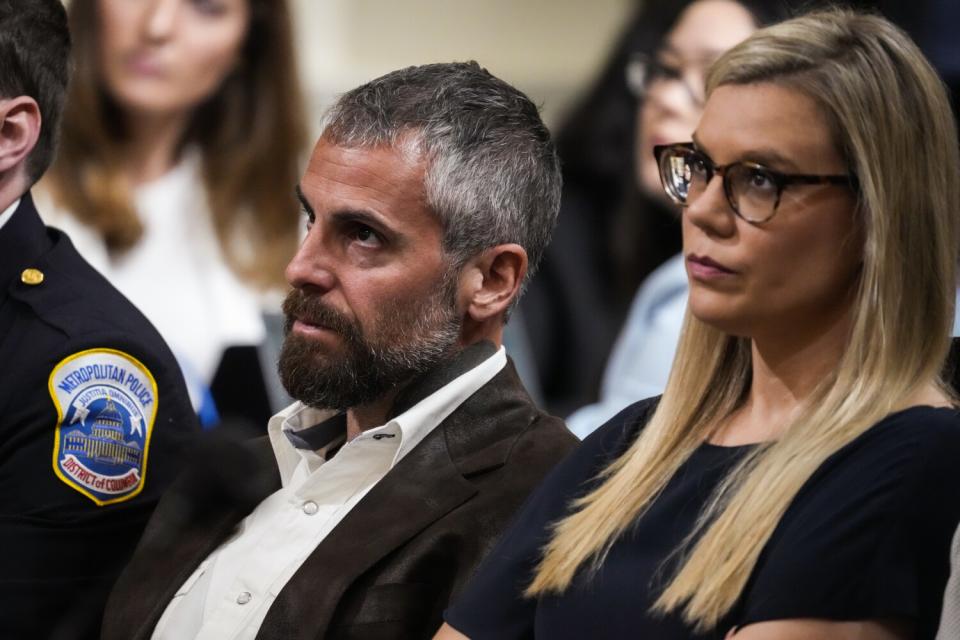 A man and woman sitting at a hearing with serious faces