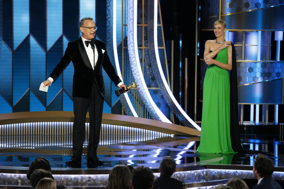 This image released by NBC shows Tom Hanks accepting the Cecil B. DeMille Award as presenter Charlize Theron looks on at right at the 77th Annual Golden Globe Awards at the Beverly Hilton Hotel in Beverly Hills, Calif., on Sunday, Jan. 5, 2020. (Paul Drinkwater/NBC via AP)