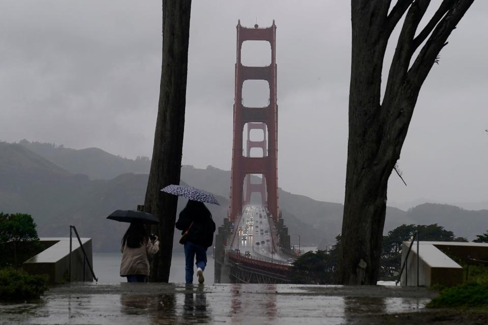 Traffic moves on the Golden Gate Bridge as people carry umbrellas while walking down a path at the Golden Gate Overlook in San Francisco, March 9, 2023. California is bracing for the arrival of an atmospheric river that forecasters warn will bring heavy rain, strong winds, thunderstorms and the threat of flooding even as the state is still digging out from earlier storms. (AP Photo/Jeff Chiu)