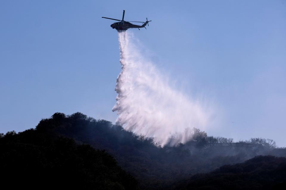 A A helicopter makes a water drop to put out hotspots in a wildfire in Topanga, west of Los Angeles, Monday, July 19, 2021.