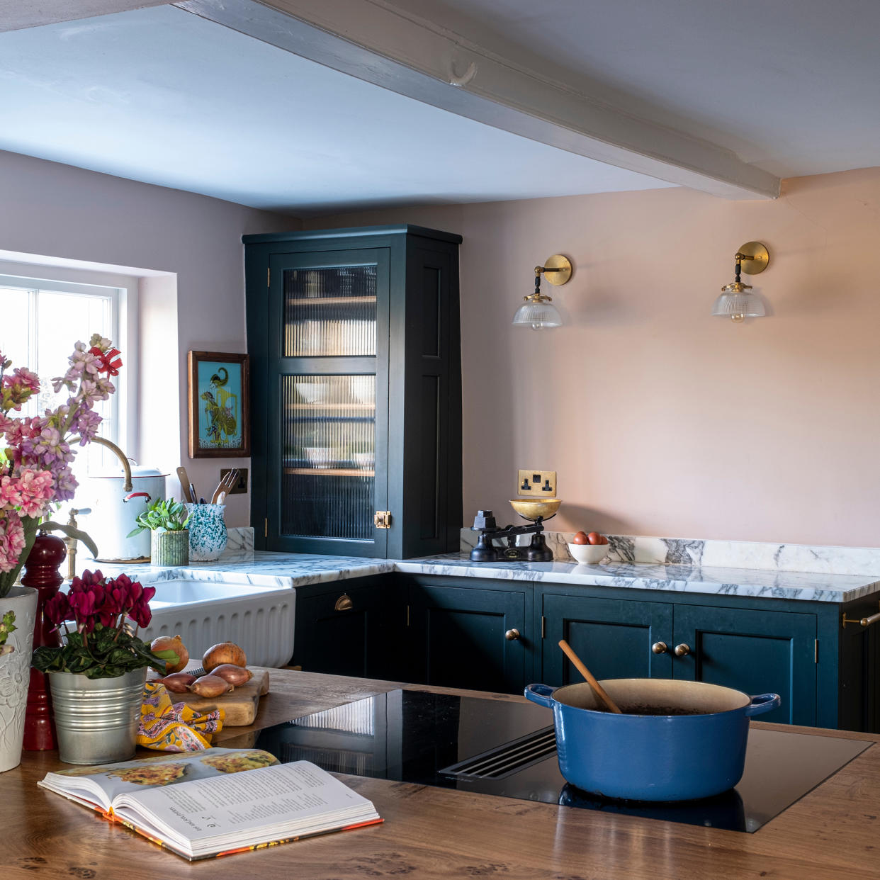  Belfast sink in fromt of a window in a small kitchen with poink walls and dark green cabinets. 