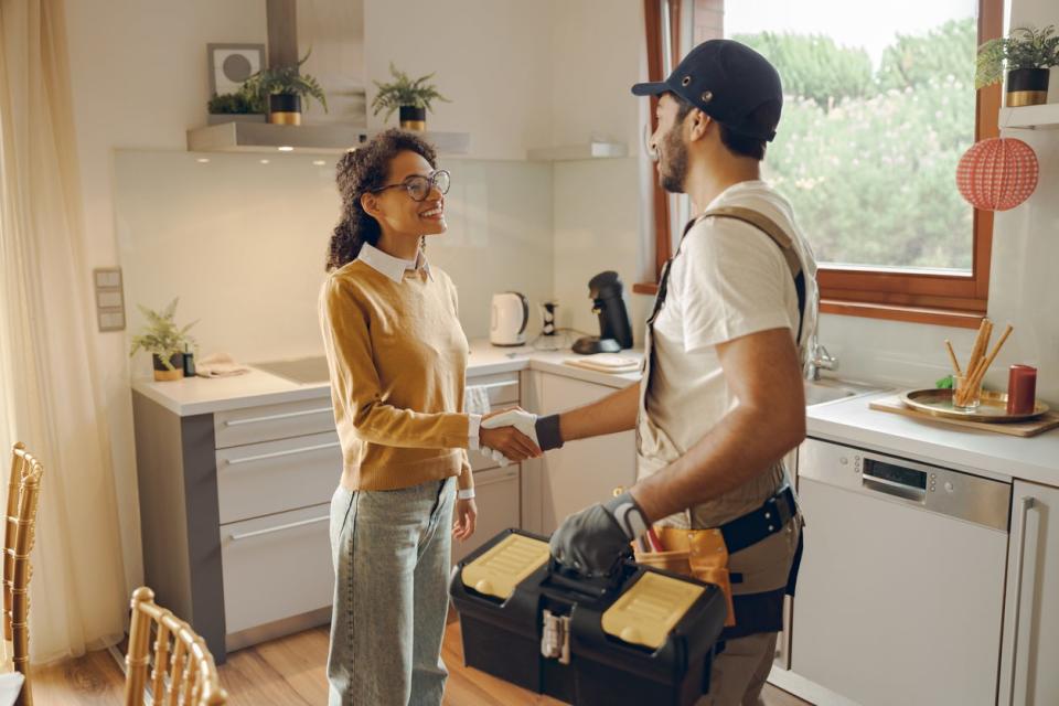 A man with a tool box and a woman shake hands in a kitchen.