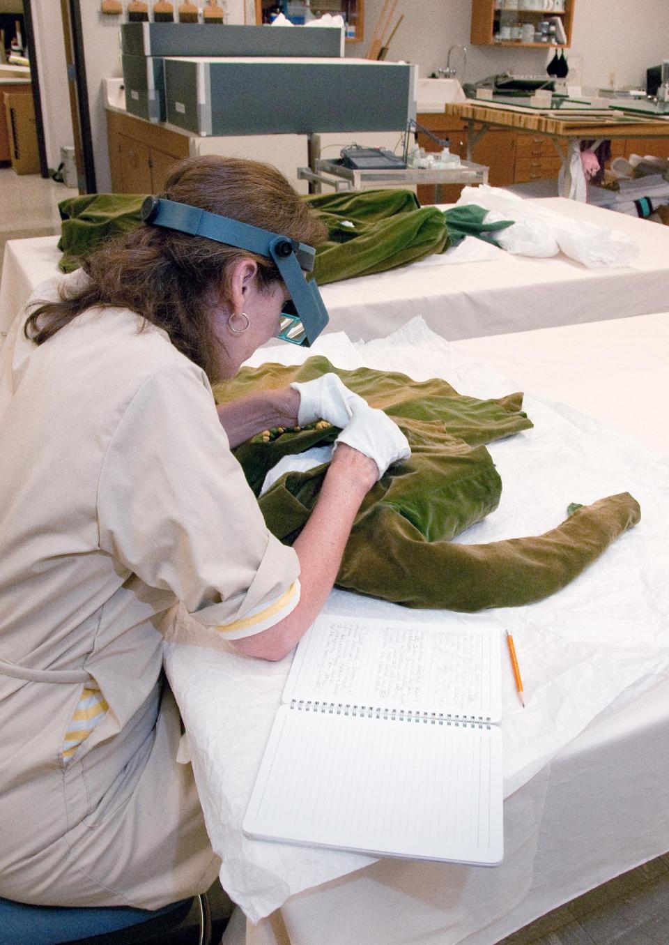 This undated handout photo provided by the Harry Ransom Center shows conservator Cara Varnell using an opti-visor, to study the green curtain dress jacket worn by Vivien Leigh as Scarlett O'Hara in "Gone With the Wind". The iconic dress and Scarlett's burgundy ball gown from the 1939 film were saved from deterioration by a $30,000 conservation effort by the Harry Ransom Center at the University of Texas. The dresses are on display for the first time in nearly 30 years at London's Victoria and Albert Museum as part of a Hollywood costume exhibit. (AP Photo/Harry Ransom Center,Pete Smith)