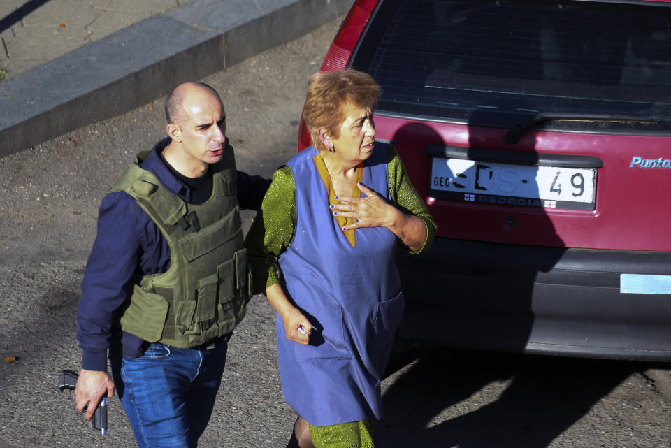 A Georgian police officer escorts a woman who escaped from a bank where an armed assailant has taken several people hostage, in the town of Zugdidi in western Georgia, Wednesday, Oct. 21, 2020. An armed assailant took several people hostage at a bank in the ex-Soviet nation of Georgia on Wednesday, authorities said. The Georgian Interior Ministry didn't immediately say how many people have been taken hostage in the town of Zugdidi in western Georgia, or what demands the assailant has made. Police sealed off the area and launched an operation "to neutralize the assailant," the ministry said in a statement. (AP Photo/Zurab Tsertsvadze)