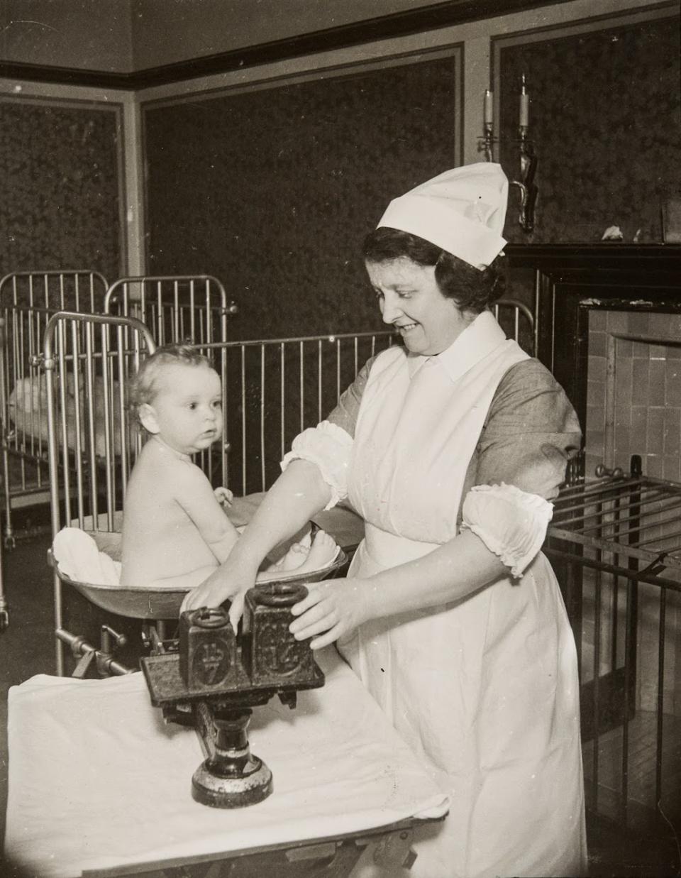 A nurse weighing a baby on a set of balance scales, at the St Matthew’s Hospital Nursery School at Tyseley, Grimms Hill, Great Missenden, Buckinghamshire