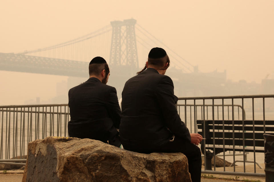 <p>Two Orthodox Jewish men sit by the waterfront as haze and smoke caused by wildfires in Canada cover the Manhattan Skyline, in Brooklyn, New York, United States, June 7, 2023. REUTERS/Amr Alfiky</p> 