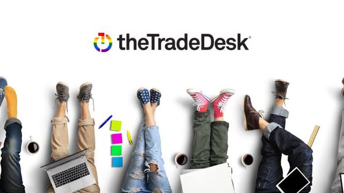 Several legs and feet of people with laptops, on a graphic bearing The Trade Desk's logo