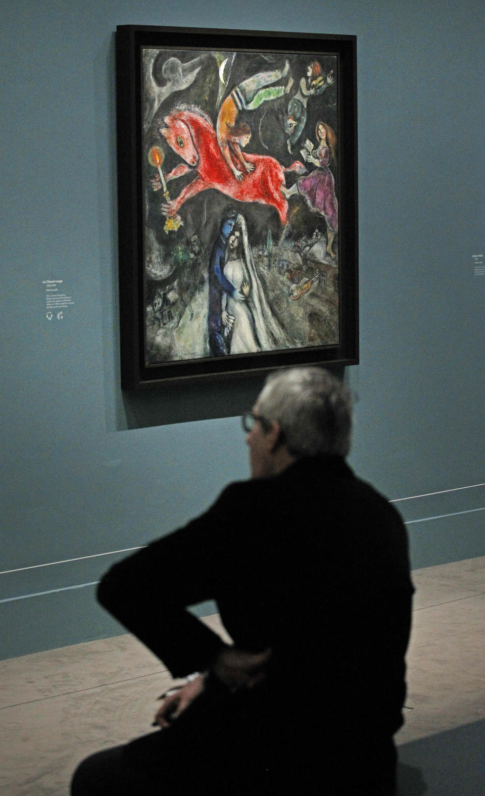 A member of the media sits next to 1944, Le Cheval Rouge, a painting by Russian artist Marc Chagall before the opening of the exhibition: Chagall, between War and Peace, at the Luxembourg museum in Paris, Tuesday Feb. 19, 2013. The exhibition starts February 21 and ends July 21, 2013.(AP Photo/Remy de la Mauviniere)