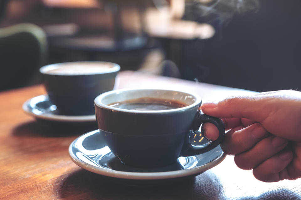 Closeup image of a hand holding a blue cup of hot coffee with smoke on wooden table in cafe